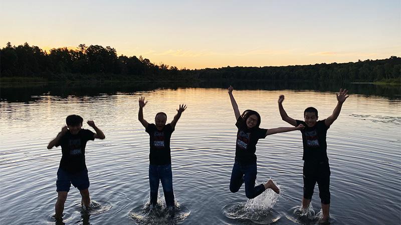 Chinese 访问ing Scholar and Interns on a northern Minnesota lake, jumping cheerfully in the air during the sunset.  