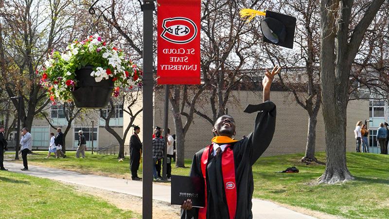 St. Cloud State University graduate throwing cap in the air under a St. Cloud State University banner